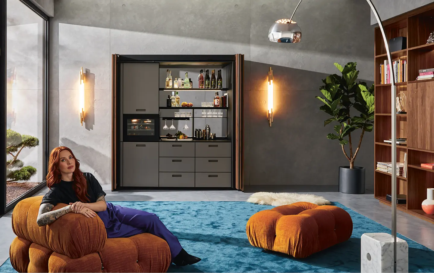 Tattovierte Frau auf Sitzkissen in kompakt verstaubarer Kueche in geraeumigem Wohnbereich.