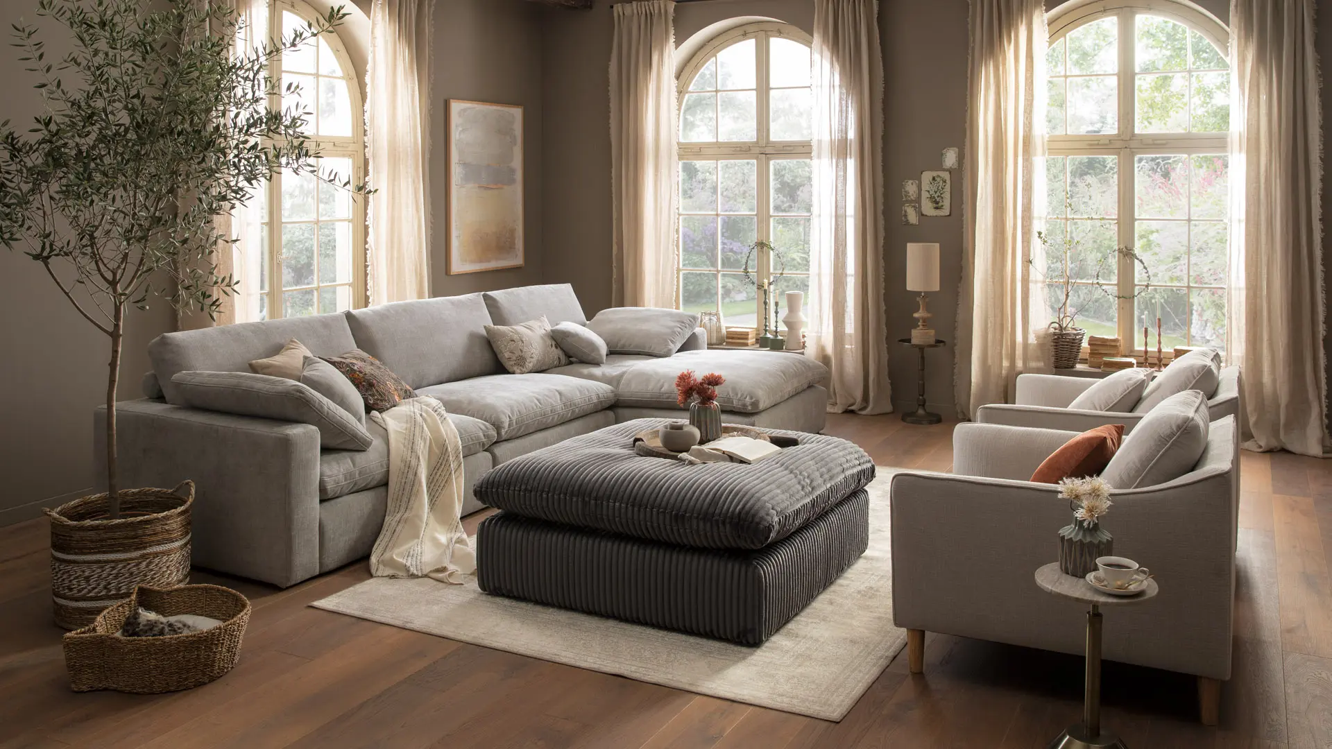 lebensart Palmdale graues großes Ecksofa in einem gemütlichen Wohnzimmer mit zwei Sesseln und Hocker in Cord.