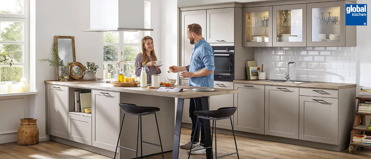Global Küchen - Paar in brauner Landhausküche mit Kücheninsel und Barhockern