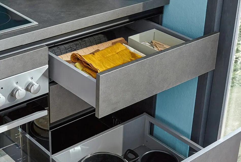 Geöffnete Küchenschublade mit Stauraum neben Backofen in kleiner Küche.
