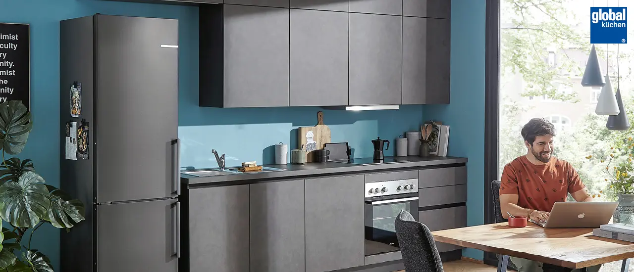 Global Küchen - Mann an Esstisch sitzend vor minimalistischer anthrazitfarbener Küchenzeile
