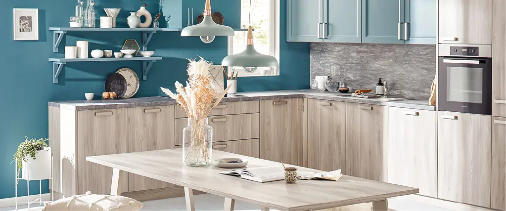 Helle Wohnküche mit Einbauküche in Holzoptik, offenen Regalen und Essgruppe mit Tisch und Bänken. Moderne Küche mit gemütlicher Sitzgelegenheit, Dekoration und viel Tageslicht für gemeinsames Kochen und Essen.