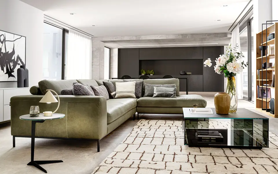 Wohnzimmer Ansicht mit Ledercouch in olivegrün und gläsernen Couchtisch.
