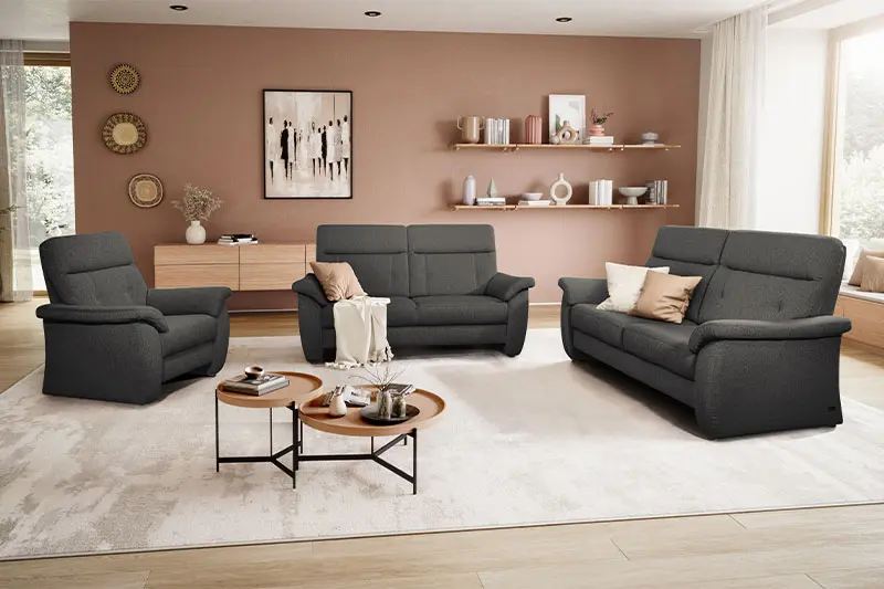 Grauer Sessel, neben zwei grauen Couch Garnituren in einem hellen gemütlichen Raum.