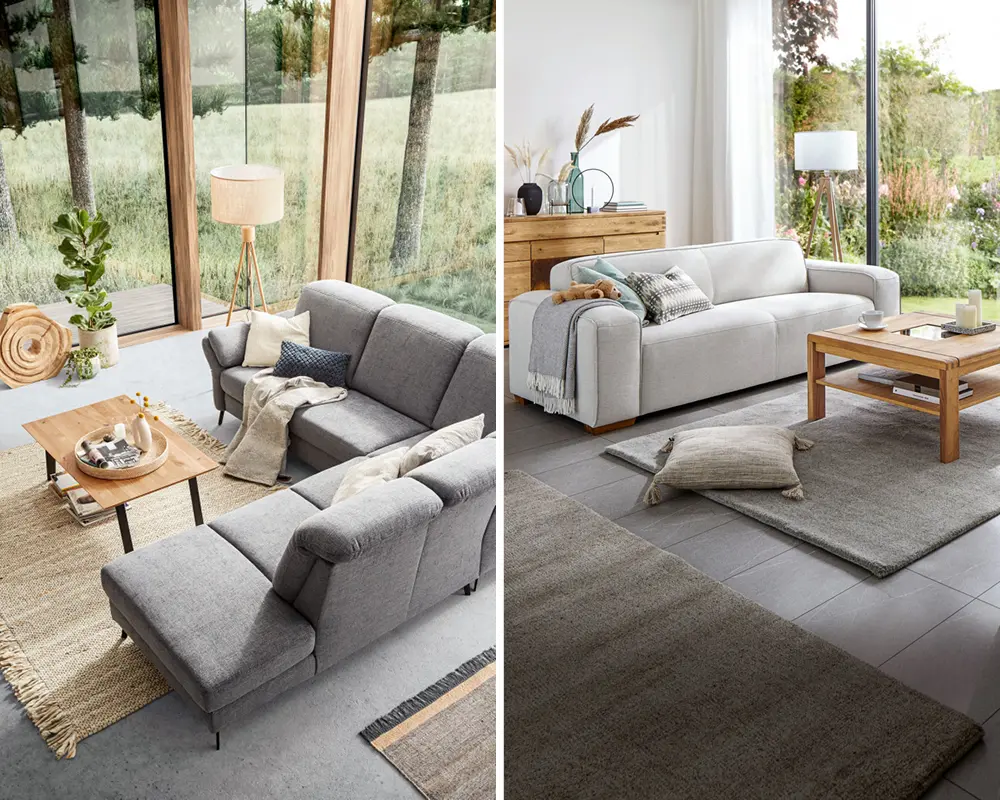 NATURA HOME Sofas im hellen Wohnzimmer mit großen Fenstern, Mann am Fenster neben einer NATURA HOME Wohnwand