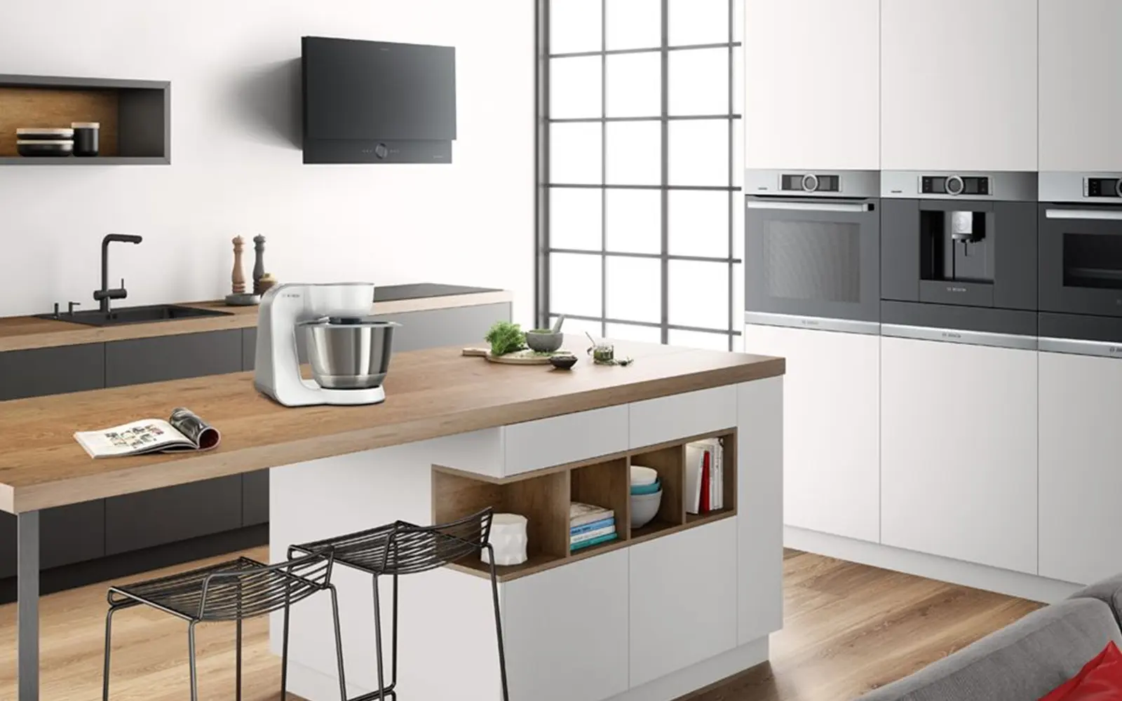 Moderne Küche mit Küchenzeile, Hochschränken mit Backofen, Kaffeemaschine und Dampfgarer und einer Kücheninsel. Weiße Fronten und Holzarbeitsplatten.&nbsp;