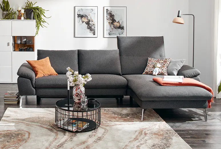 Dunkelgraues Sofa mit hoher Rückenlehne auf hellem Teppich, Frau auch grauer Couch mit hoher Rückenlehne im hellen Wohnzimmer, elegante, kognacfarbene Ledercouch mit aufgestellter Rückenlehne auf edlem Holzfußboden