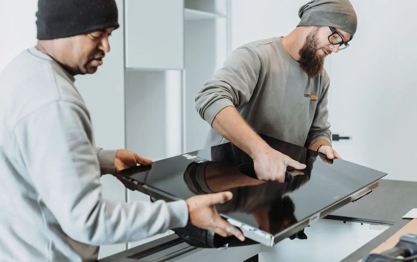 Montagemitarbeiter von Moebel Erfurth bauen Herdplatte in Kueche ein