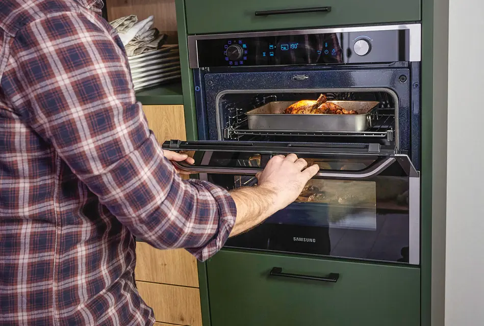 Mann öffnet Einbaubackofen mit Braten in kompakter Küche.