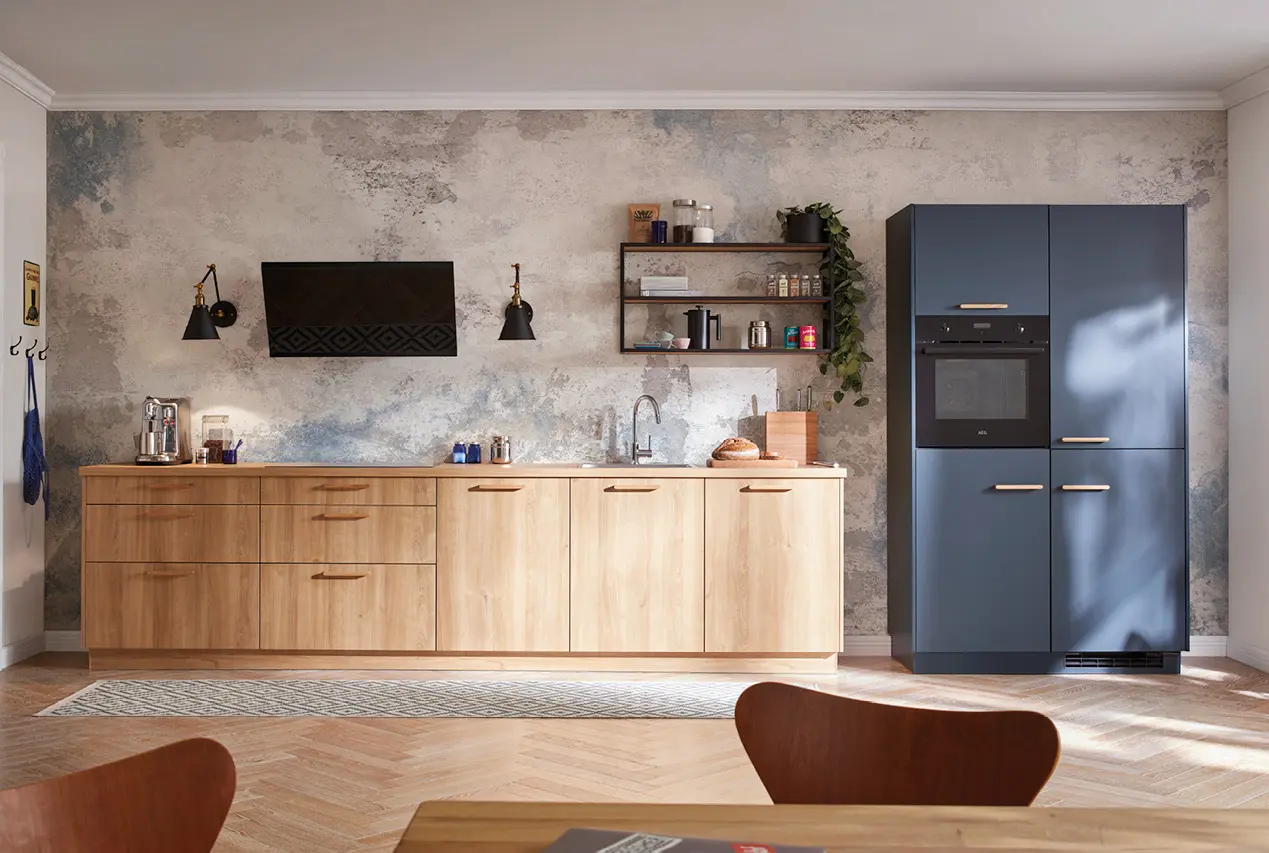 Moderne Küche mit hellen Holzfronten, blauen Hochschränken und integrierten Elektrogeräten. Klare Linien, offene Regale und strukturierte Wandfläche schaffen ein hochwertiges Küchendesign für zeitgemäßes Wohnen.