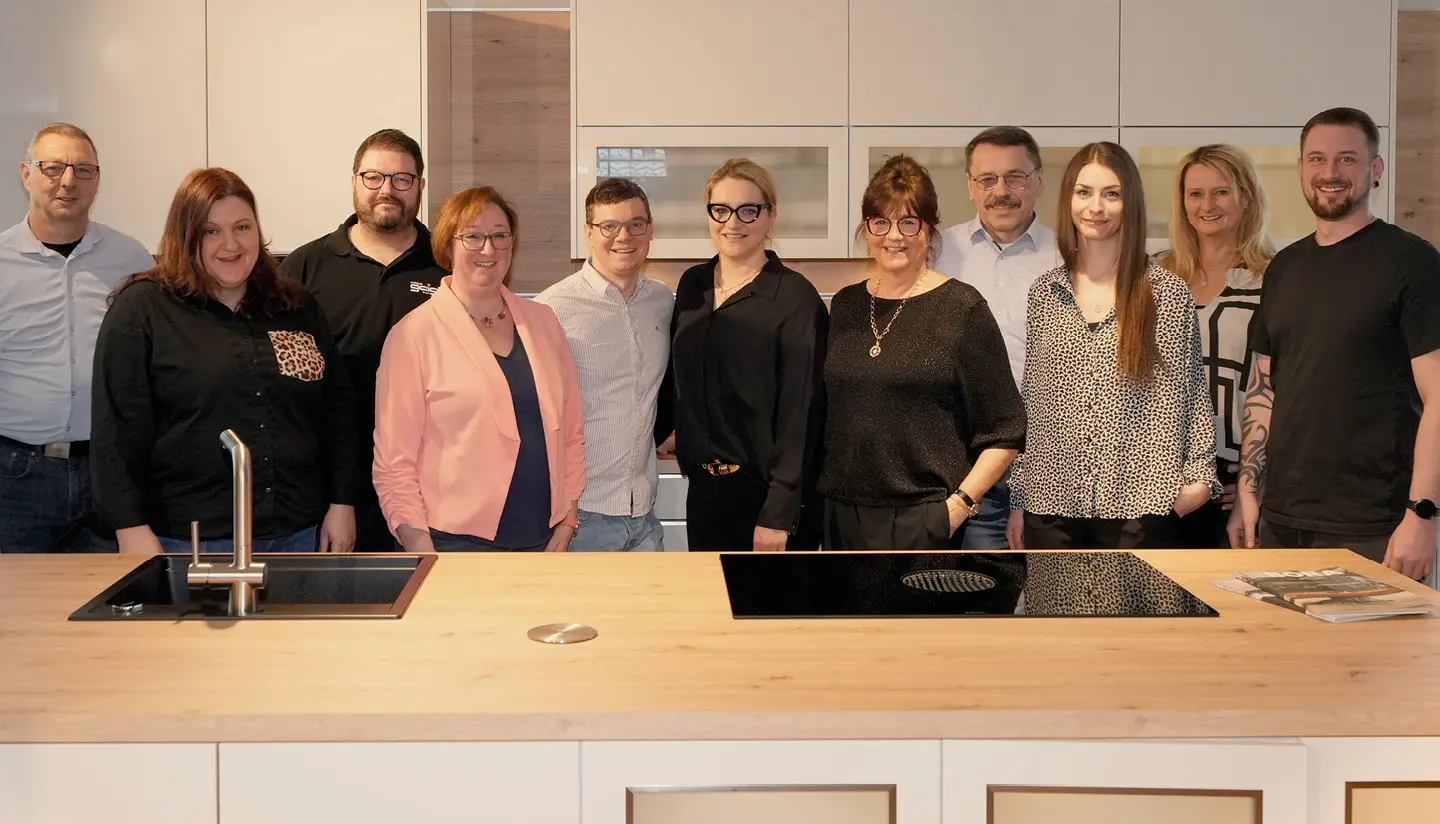 Das Team von Möbel Geigl hinter Kücheninsel im Möbelhaus