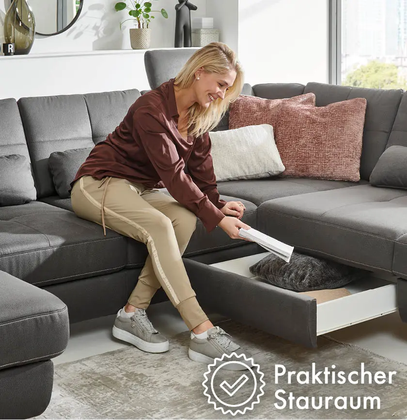 Frau legt Buch in Stauraum unter dem grauen Sofa