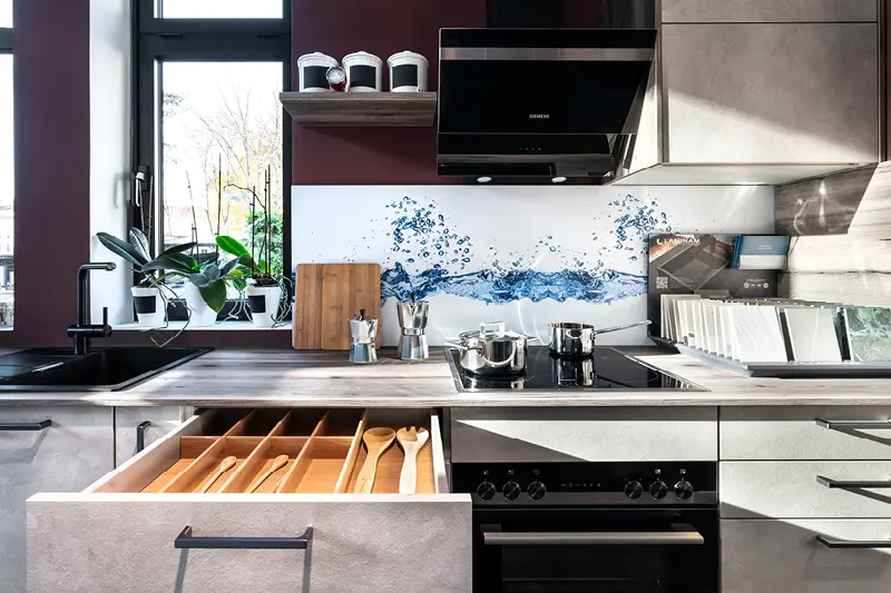 Helle Contur Kuechenzeile mit geoeffneter Schublade und Dunstabzugshaube.