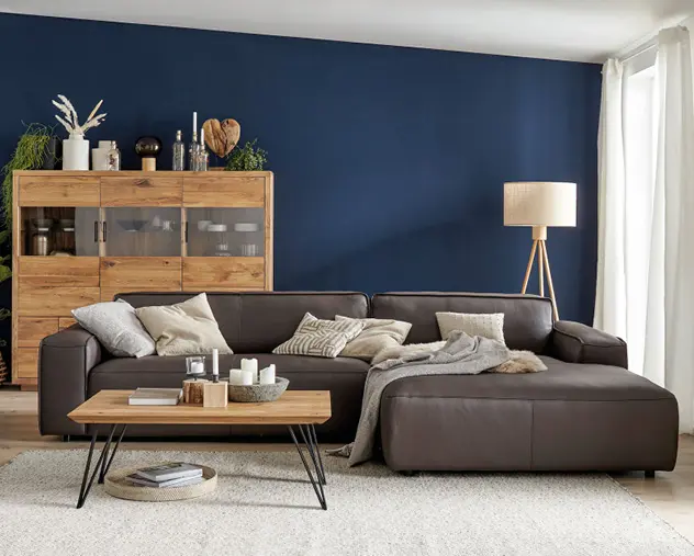 Dunkelbraunes Ledersofa vor blauer Wand mit Holzsideboard und Couchtisch