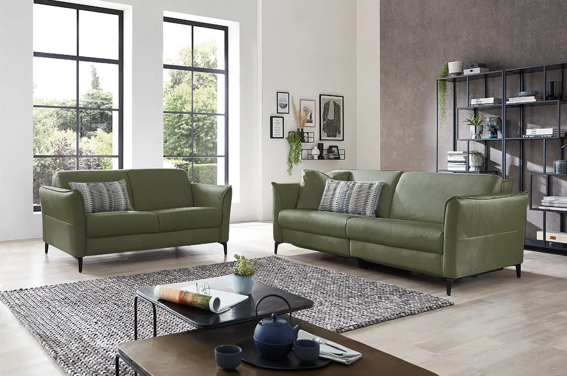 Zwei olivgrüne Sofa Garnituren in einem hellen gemütlichen Raum.