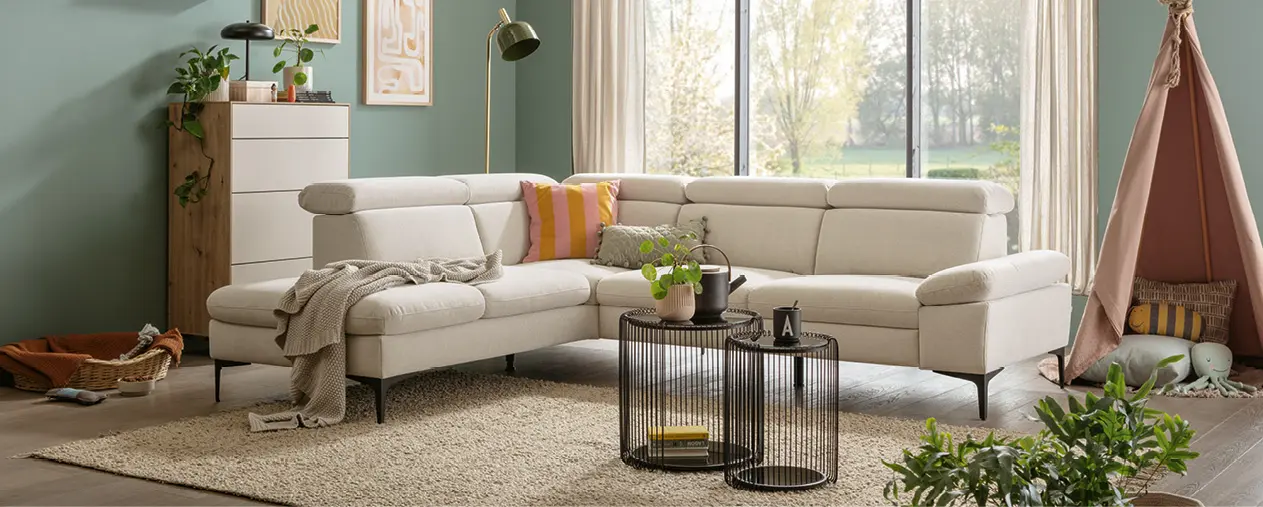 Helles modernes Wohnzimmer mit großzügigem Ecksofa, Teppich, Beistelltischen und Pflanzen. Wohnliche Einrichtung mit natürlichem Licht, ideal für stilvolles Wohnen, Sofalandschaft und gemütliche Wohnideen.
