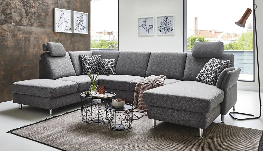 Ecksofa in dunklem Grauton von Couchliebe mit verstellbaren Kopfstützen und gemusterten Kissen in modernem Wohnzimmer – erhältlich bei Möbel Rommel.