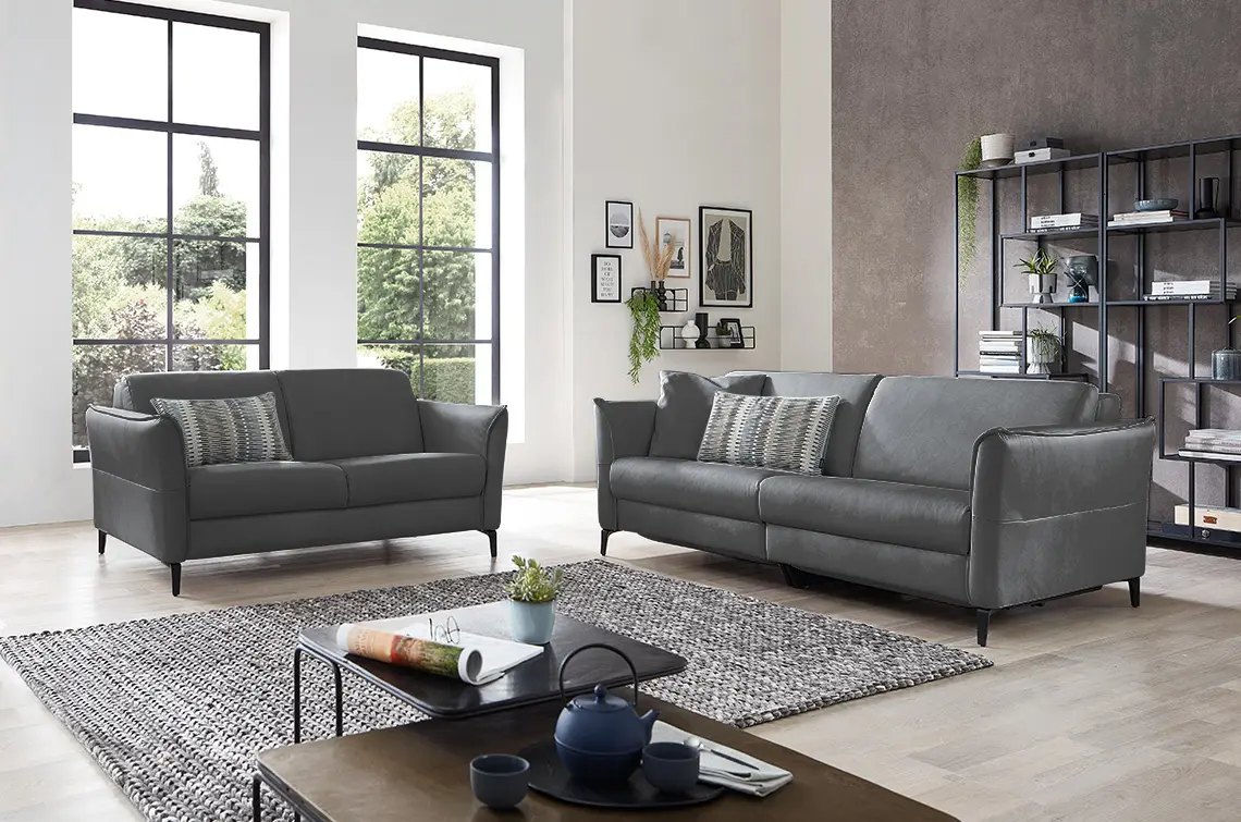 Zwei dunkelgraue Sofa Garnituren in einem hellen gemütlichen Raum.