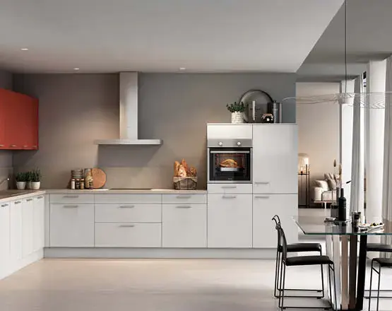 Weiße Eckküche mit Backofen, hohen Schränken und grauer Arbeitsplatte, vor Fenster mit Pflanzen und hellem Teppich.