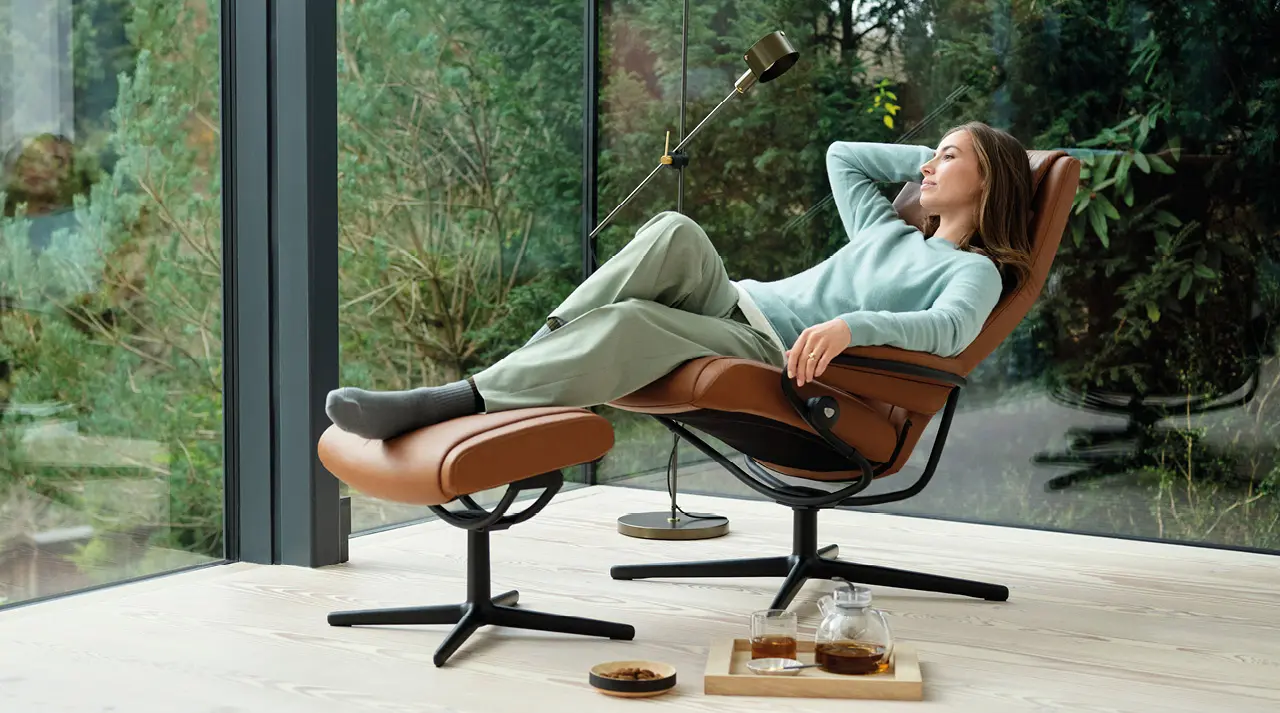 Frau entspannt im Stressless Relaxsessel mit Hocker am Fenster
