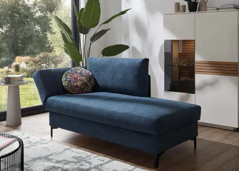 Blaues Schlafsofa mit rundem Kissen, Pflanze und weißem Schrank im Wohnzimmer