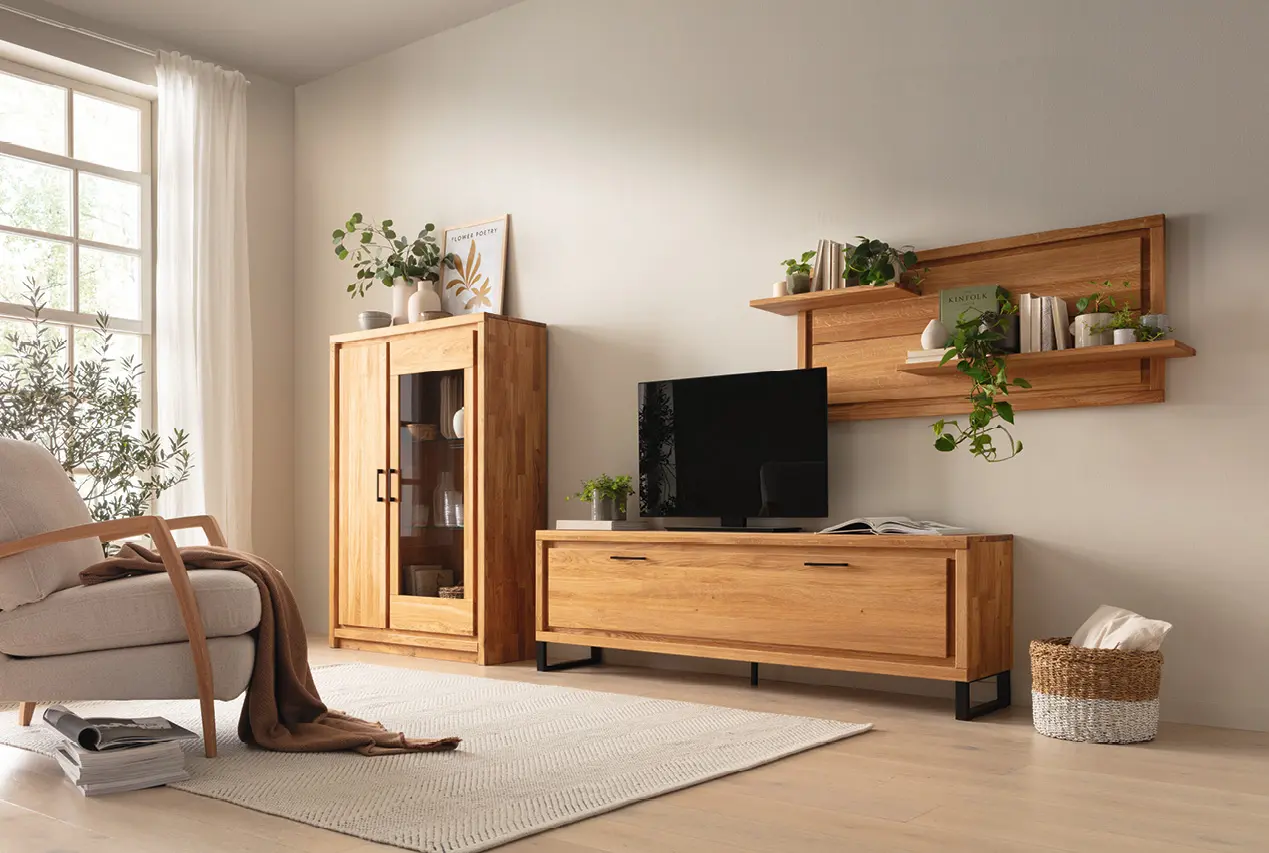 Helles Wohnzimmer mit Massivholzmöbeln aus Eiche, TV Lowboard, Vitrine und Wandregal, kombiniert mit Pflanzen, Sofa und Teppich für ein modernes, natürliches Wohnambiente mit warmen Farben