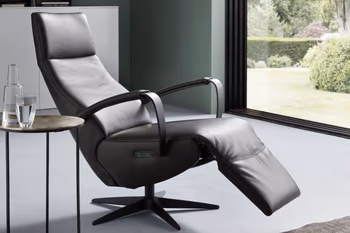 Relaxsessel mit offenen Armlehnen und leicht nach oben geklappter Fußlehne mit braunem Lederbezug.