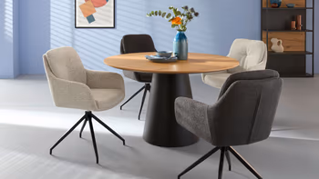 Helles Wohnzimmer mit rundem Tisch und vier verschiedenfarbigen Sesseln. 