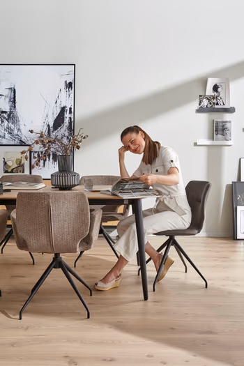 Grauer moderner Armlehnstuhl, der an einem Wildeiche Esstisch steht, an dem eine Frau sitzt.
