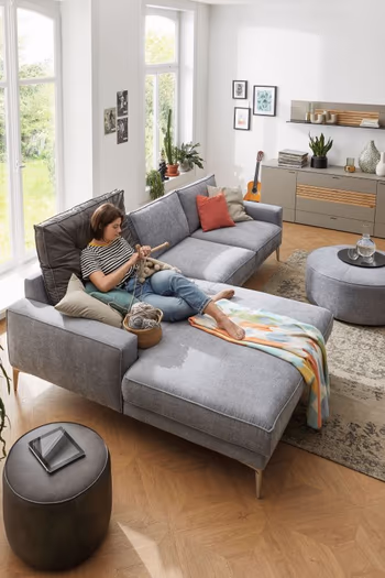 Gemütliches graues Ecksofa, auf dem eine Frau liegt.