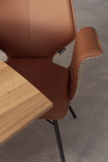 Moderner Design Esszimmerstuhl mit Armlehne, der auf der Innenseite einen Lederbezug in rose hat und leicht weggedreht von einem Holztisch steht.