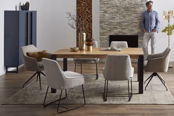 Moderner Massivholz Esstisch, um den herum graue Schalenstühle stehen in einem hellen Raum in dem ein Mann an einer Wand lehnt.