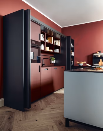 Eine Pocket-Küche von next125 mit roten Fronten und schwarzen Korpussen. Vor der Küche steht eine Insel mit weißer Verkleidung.&nbsp;