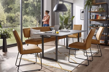 Sitzbank und Stühle mit gelbem Leder und schwarzem Metallgestell um einen modernen Esstisch.