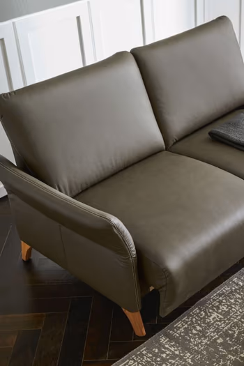 Dunkelgrünes Sofa mit großen Rückenkissen und leicht nach außen geneigter Armlehne mit Holzbeinen.