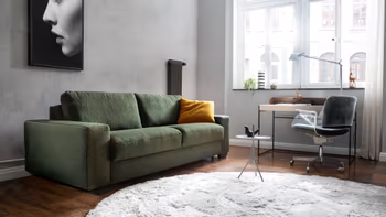 Grünes Zweisitzersofa in einem hellen Raum, mit einem gelben Kissen auf der rechten Seite.