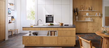 Helle hoelzerne Inselkuche vor weisser Kuechenzeile.