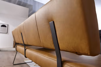 Rückseite einer cognac farbenen Rückenlehne einer Sitzbank, die Rückenlehne ist mit hochkanten schwarzen Metallstreben an der Bank befestigt.