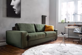 Grünes Zweisitzersofa in einem hellen Raum, mit einem gelben Kissen auf der rechten Seite.