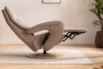 Seitliche Aufnahme eines beigen Relaxsessels, der sich in Liegeposition befindet in einem hellen Zimmer mit cremefarbenem Teppich und einer kleinen Palme.