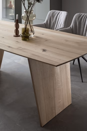 Moderner Massivholz Esstisch mit Fußgestell aus Massivholz, auf dem 2 Vasen und ein Kerzenständer stehen.