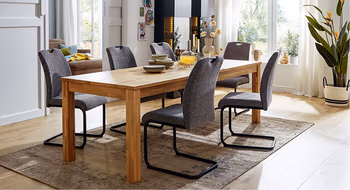 Schicke Esszimmereinrichtung mit Massivholztisch und dunkelgrauen Stoffstuehlen vor schwarzem Highboard mit LED-Beleuchtung.