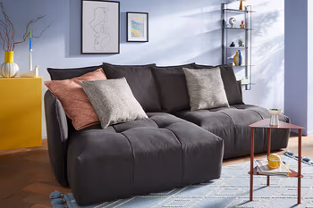 Dunkelgraues Sofa mit gemütlichen Kissen an der Rückenlehne und Dekokissen in grau und rot auf der Sitzfläche.