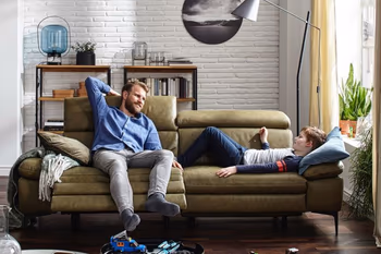 Grünes Ledersofa auf dem ein Mann sitzt und daneben ein Junge liegt.