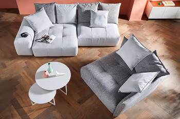 Wohnzimmer in Vogelperspektive mit grauem kleinen zweisitzer und einem grauen Sessel sowie einem runden Couchtisch. 