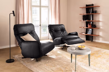 Zwei schwarze Ledersessel die nur auf jeweils einer Seite eine Armlehne haben, der rechte Sessel ist nach hinten gelehnt in Relaxposition.