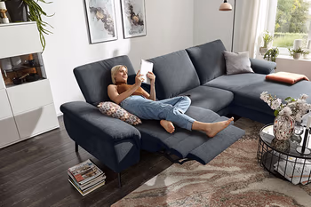 Frau entspannt auf grauem Sofa mit Relaxfunktion und liest ein Buch.