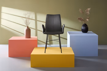 Schwarzer Armlehnstuhl mit Stativgestell auf einem gelben Podest.