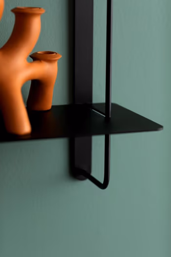 Moderne Deko in der Farbe Terrakotta auf einem schwarzen Wandregal an grüner Wand.