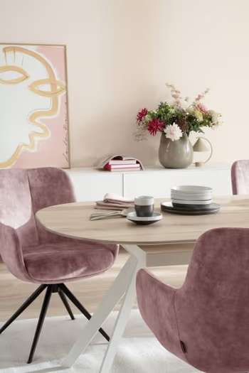 Armlehnstuhl bezogen mit Stoff in Rosa und schwarzem Metall Fußgestell an einem Esstisch mit Holztischplatte an dem ein weiterer rosa Armlehnstuhl steht.